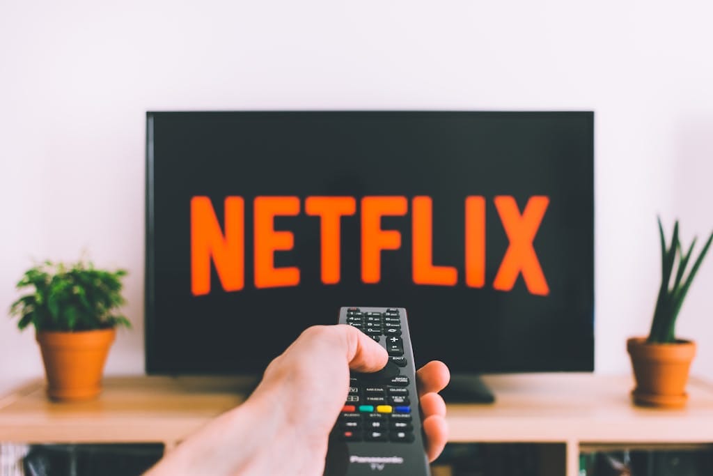 Una mano sosteniendo un control remoto de TV frente a una pantalla con Netflix, perfecto para temas de transmisión y noches de cine.