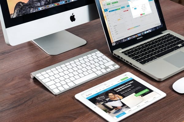 Una elegante configuración de escritorio de oficina con dispositivos Apple: iMac, MacBook y iPad.