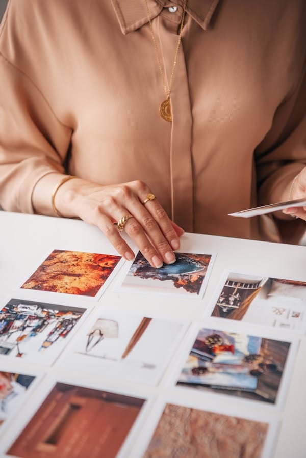 Una mujer organiza una colección de fotos de viaje vibrantes sobre una mesa blanca. Perfecto para la inspiración de viaje.