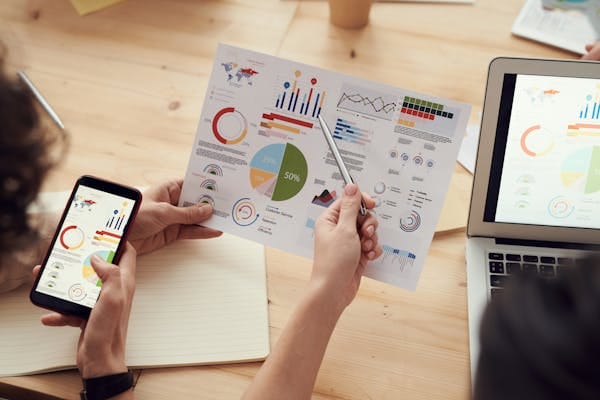 Los miembros del equipo analizan gráficos durante una reunión de negocios con portátiles y teléfonos inteligentes.
